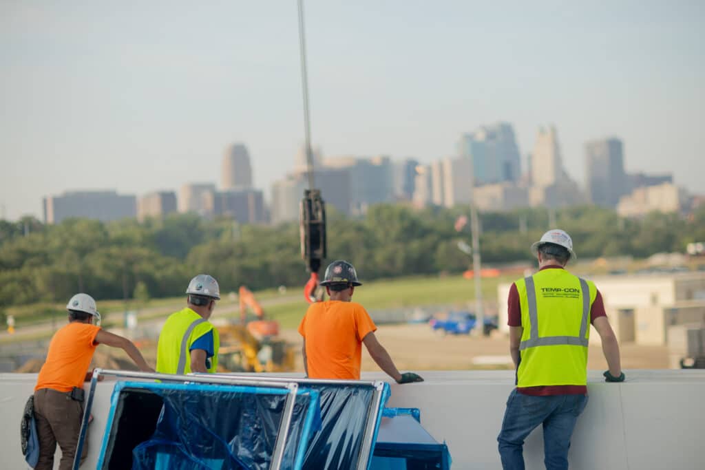 four working men standing on a job site looking at a crane with a city scape in the background