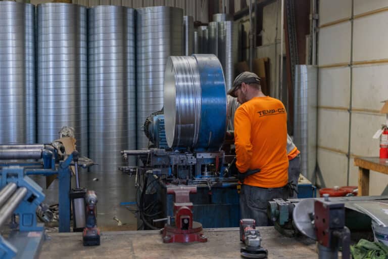 a man with an orange long sleeve shirt operating a piece of metal machinery inside