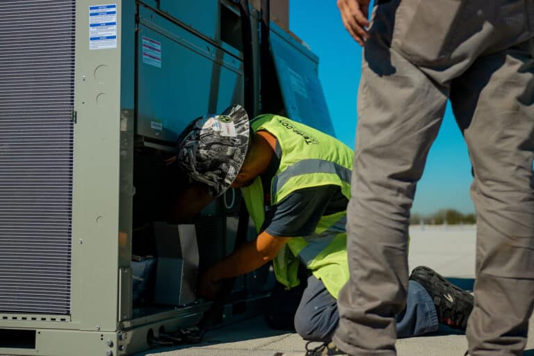 man on ground with hard hat fixing hvac unit