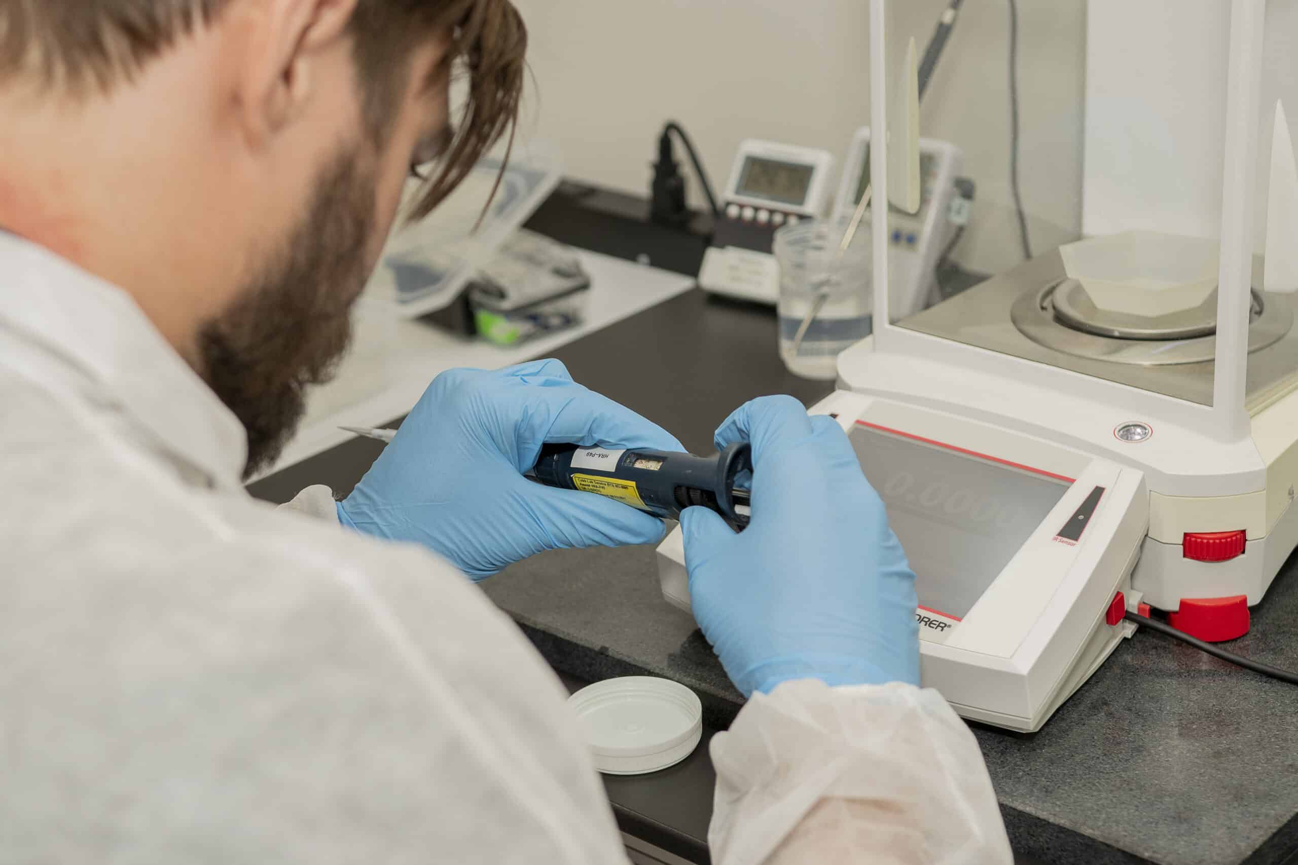 man in laboratory calibrating pipette and wearing gloves